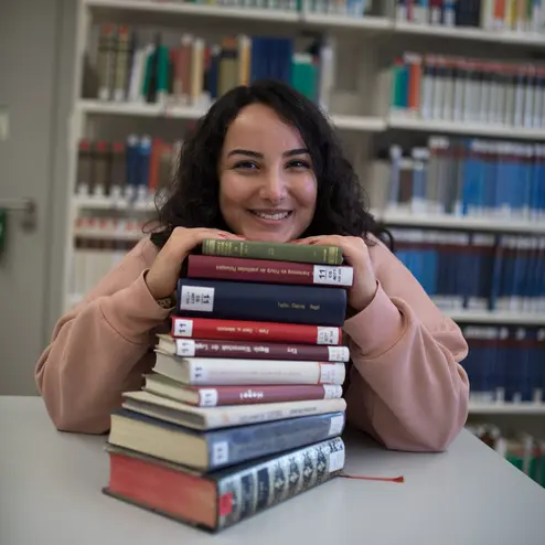 große Bücherauswahl in den Uni-Bibliotheken Studentin mit einem Stapel Bücher in der Uni-Bibliothek